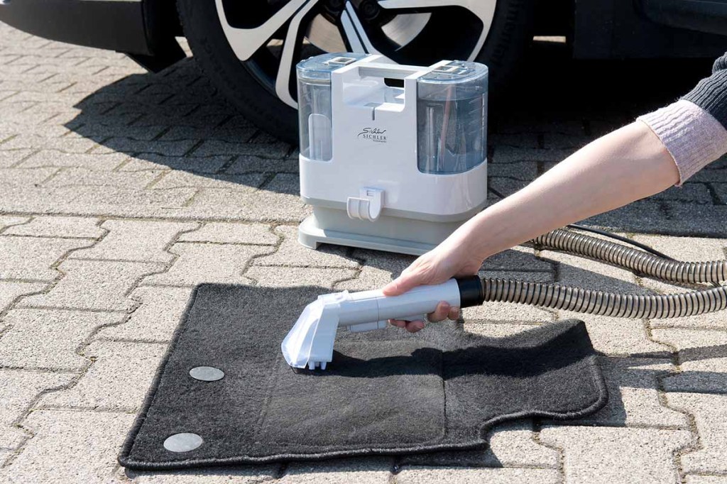 Eine Auto-Fußmatte wird mit dem Waschsauger gereinigt.