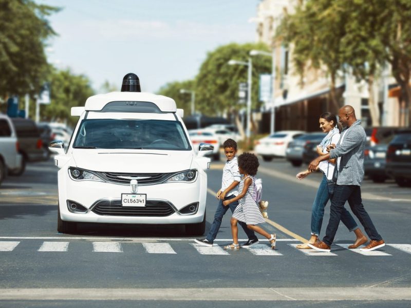 Eine Familie geht über einen Zebrastreifen, vor dem ein Waymo Fahrzeug hält.
