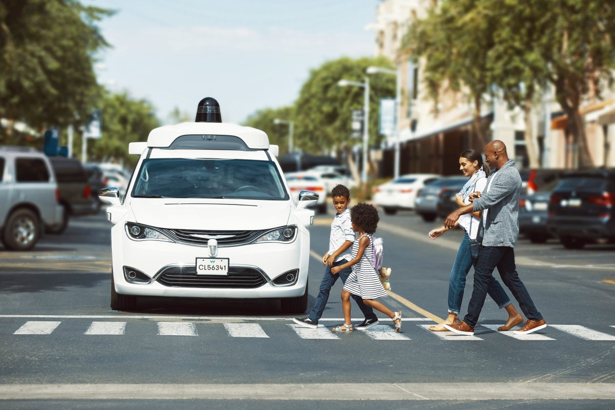 Eine Familie geht über einen Zebrastreifen, vor dem ein Waymo Fahrzeug hält.