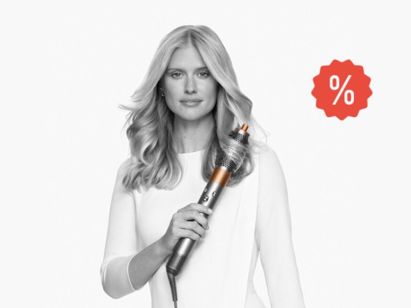 Frau von vorne hält Dyson Airwrap an Haar auf weißem Hintergrund mit rotem Prozentzeichen rechts oben