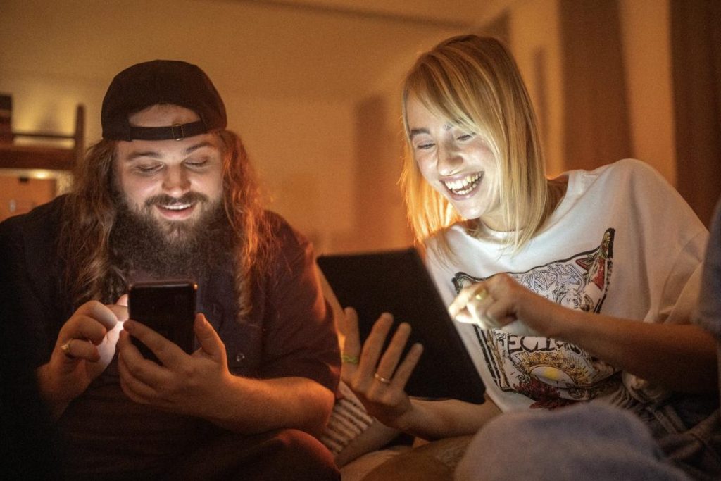 Ein Mann und eine Frau sitzen auf dem Sofa und lächeln, während sie ihre Smartphones bedienen