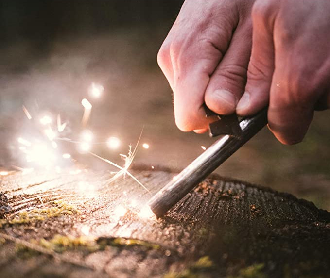 Hände halten Feuerstahl zu Boden, Funken sprühen