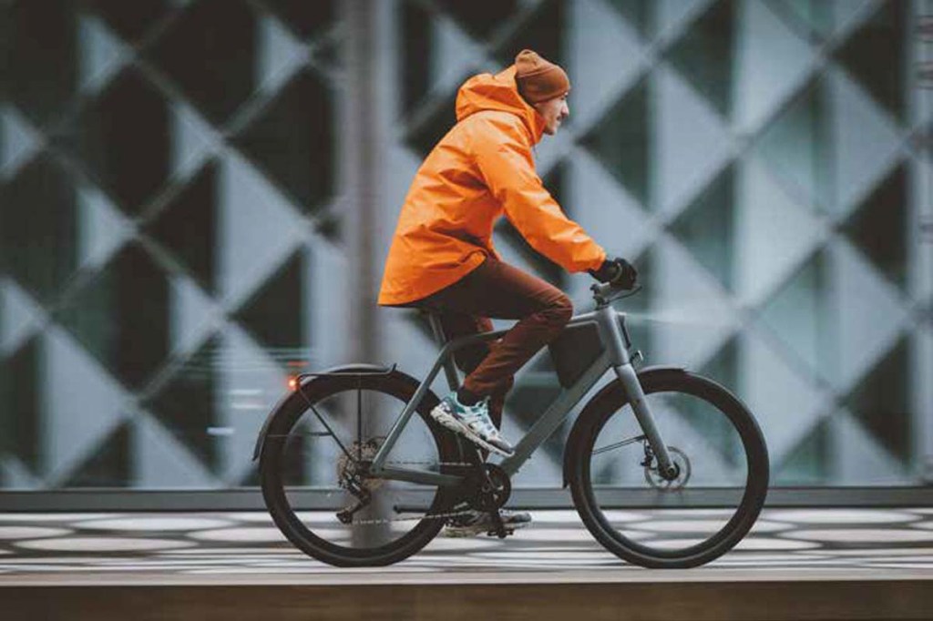 E-Biker fährt mit einem Lemo One +, in HIntergrund ist eine Kachelglaswand erkennbar