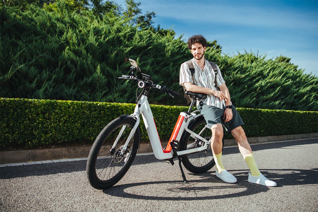 E-Bike BQi C3 auf einer Straße stehend, Mann lehnt sich cool an den Gepäckträger