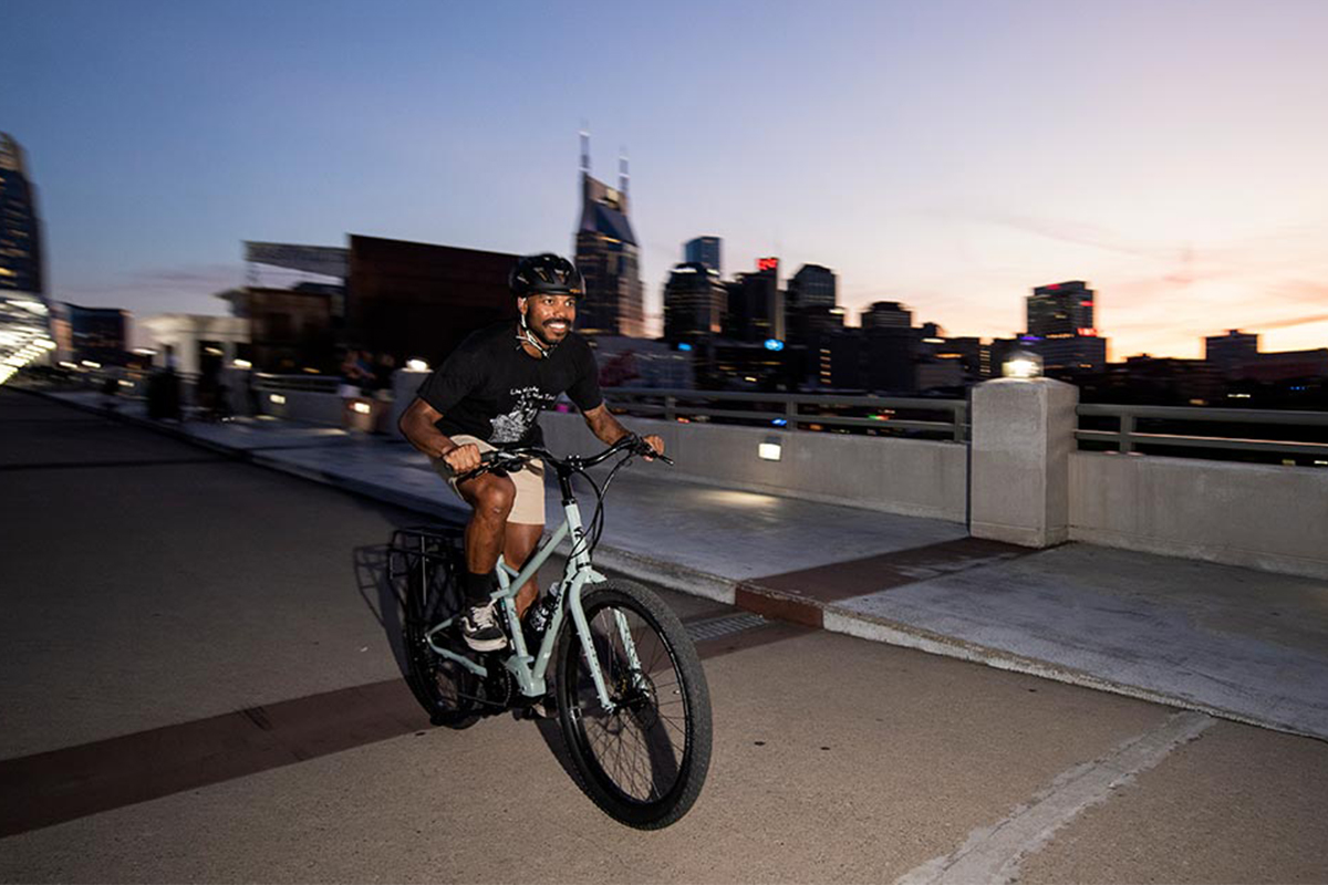 Mann fährt abends vor Großstadkulisse auf dem E-Bike Skid Loader von Surly