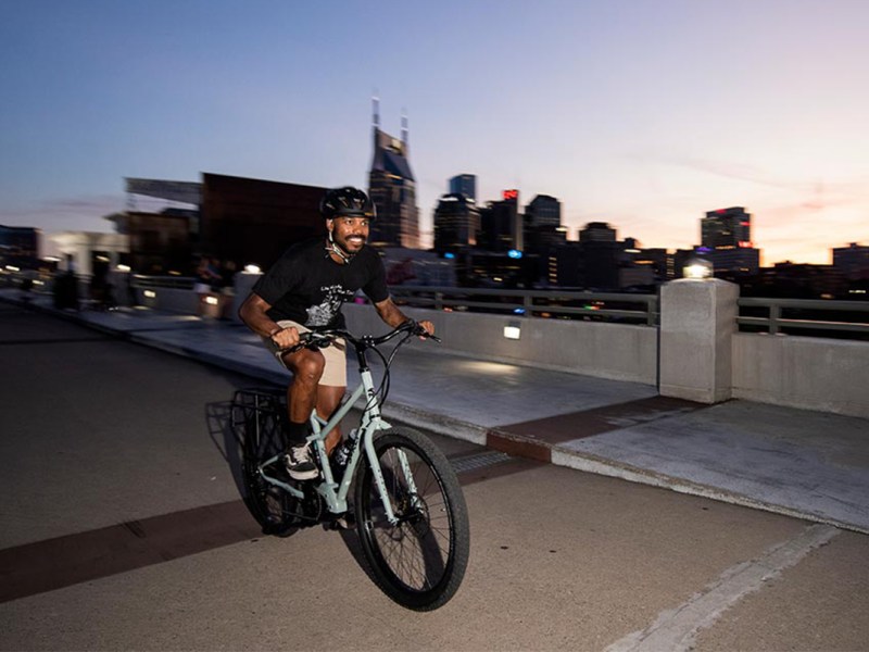 Mann fährt abends vor Großstadkulisse auf dem E-Bike Skid Loader von Surly