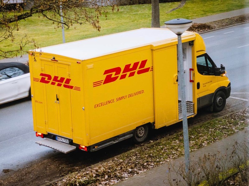 Ein DHL-Wagen parkt an einer Straße.