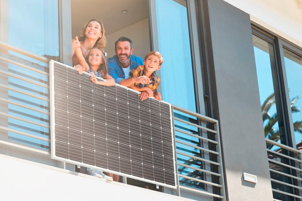 Eine junge Familie steht an einem Balkonfenster mit einem Balkonkraftwerk.