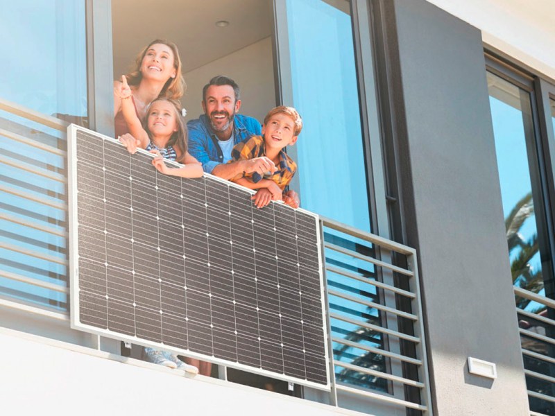 Eine junge Familie steht an einem Balkonfenster mit einem Balkonkraftwerk.