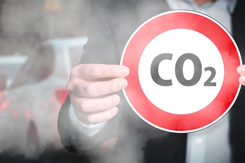 Mann vor Verkehrsszene hält Schild mit der Aufschrift "CO2" vor sich.