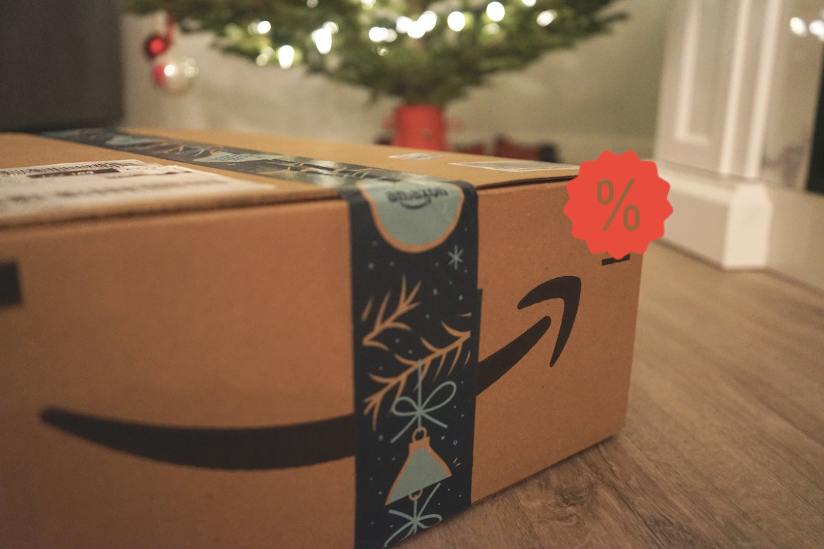 Paket von Amazon liegt auf Holzboden vor geschmücktem Tannenbaum mit rotem Prozentzeichen