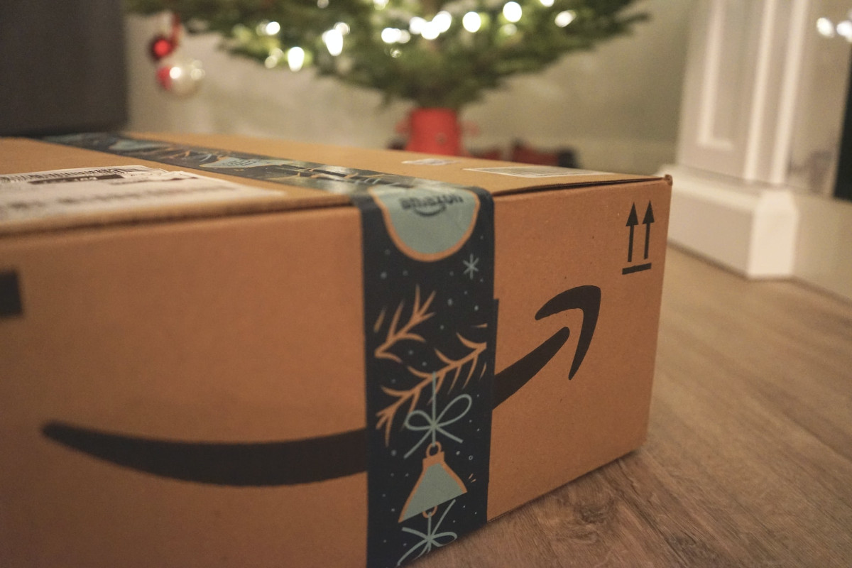 Paket von Amazon liegt auf Holzboden vor geschmücktem Tannenbaum