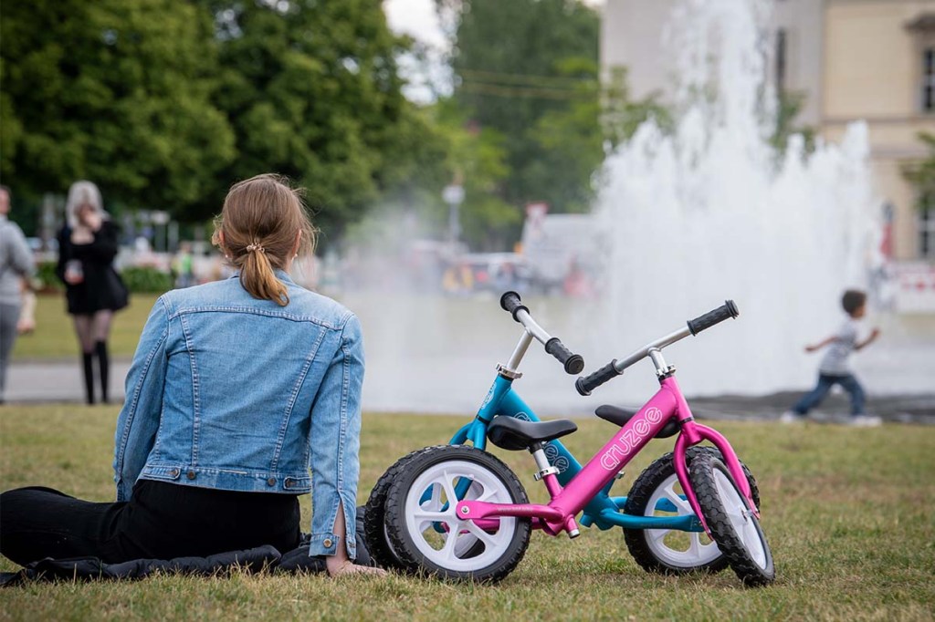 zwei Laufräder von Cruzee stehen aneinandergelehnt im Park, eine Frau sitzt daneben