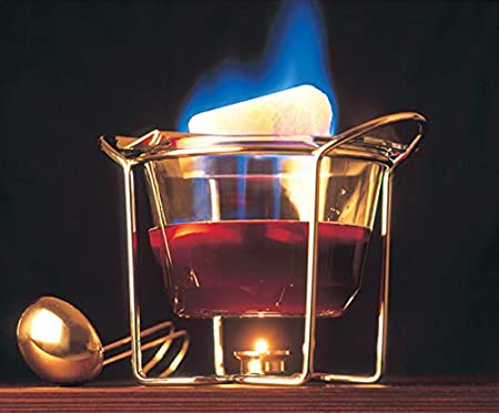 Feuerzangenbowle mit Getränk in Glasschale und brennendem Zuckerhut oben drauf vor dunklem Hintergrund