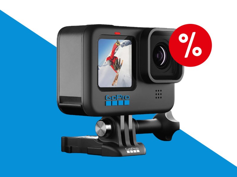 Schwarze rechteckige GoPro Hero 10 Action-Cam schräg von vorne mit Snowboader auf Display und auf schwarzer Halterung, auf blau weißem Hintergrund mit rotem Prozentzeichen rechts oben