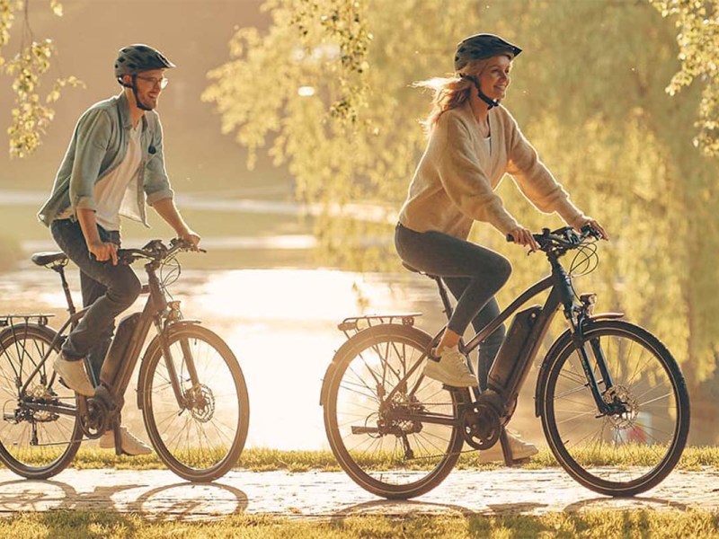Zwei Menschen auf einem E-Bike, fahren bei Sonnenschein durch die Natur