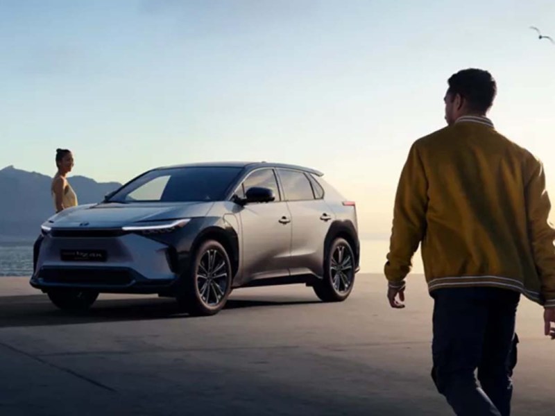 Toyota bZ Compact Concept SUV in Natur vor aufgehender Sonne, zwei Menschen laufen um das Auto herum