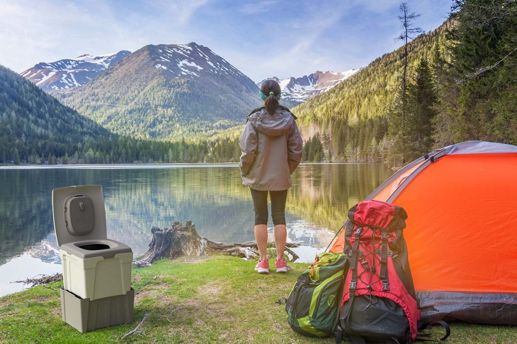 Frau steht inmitten der Natur am See, hinter ihr: ihr Zelt und ihre Campingtoilette