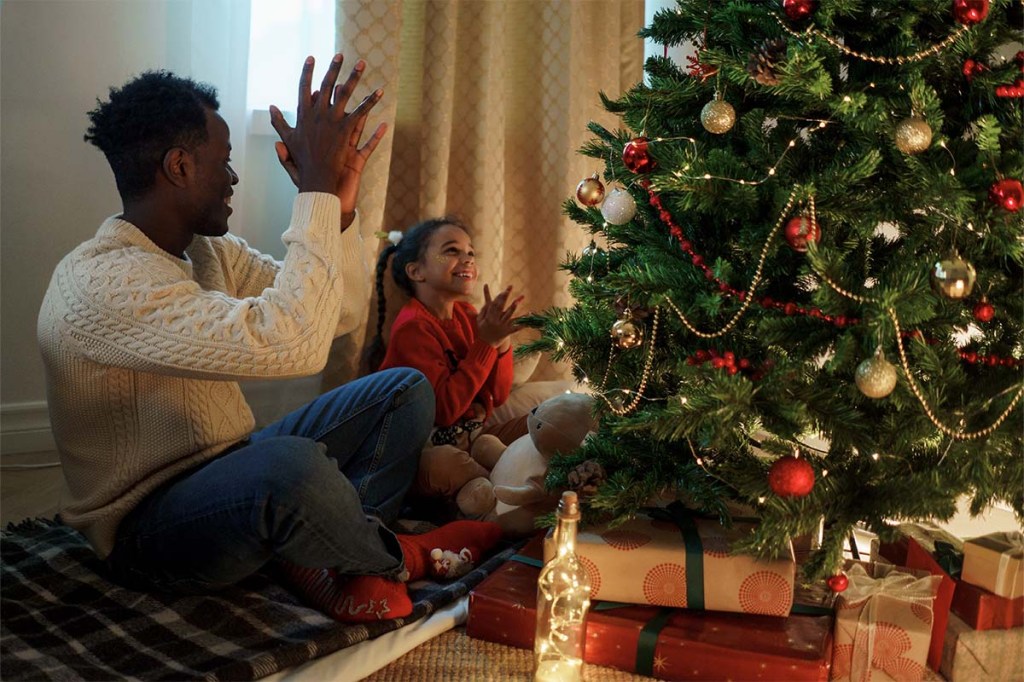 Vater und Tochter sitzen auf dem Boden vor einem geschmückten Weihnachtsbaum