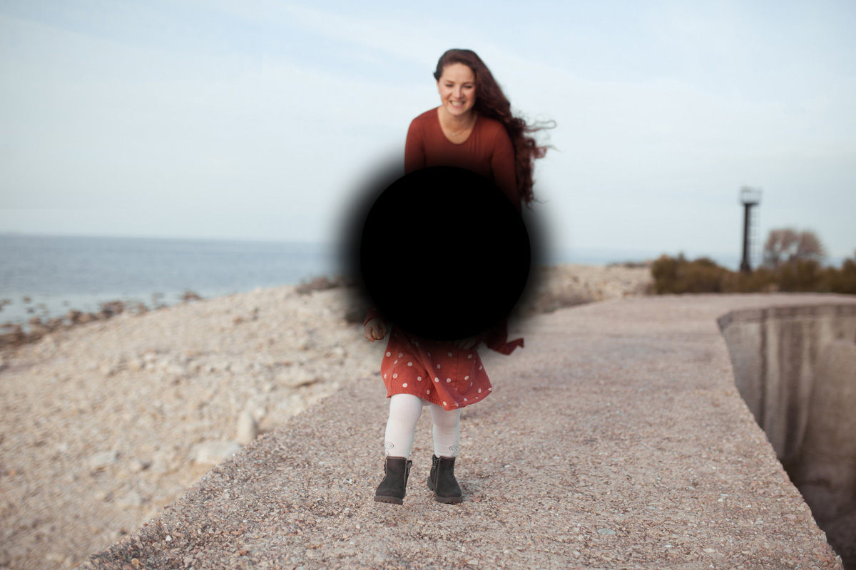 Eine Frau läuft mit einem Kind am Strand entlang, während ein Bildausschnitt aus dem Sichtfeld ist.