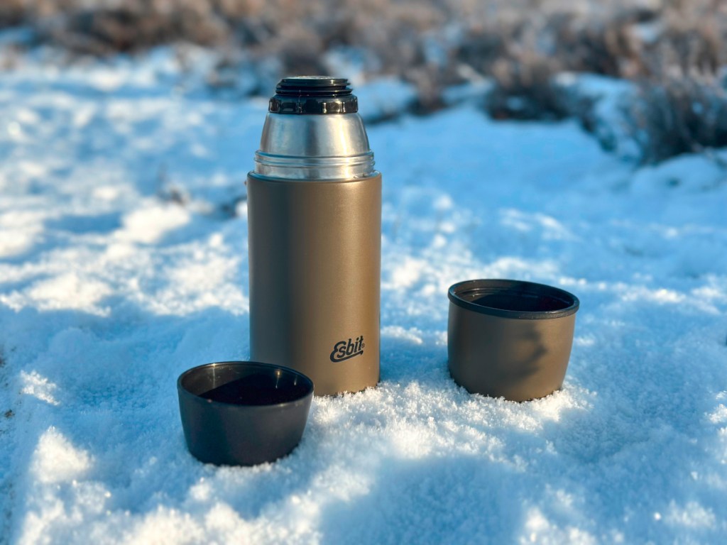 Graue Isolierflasche mit aufgeschraubtem Deckel im Schnee