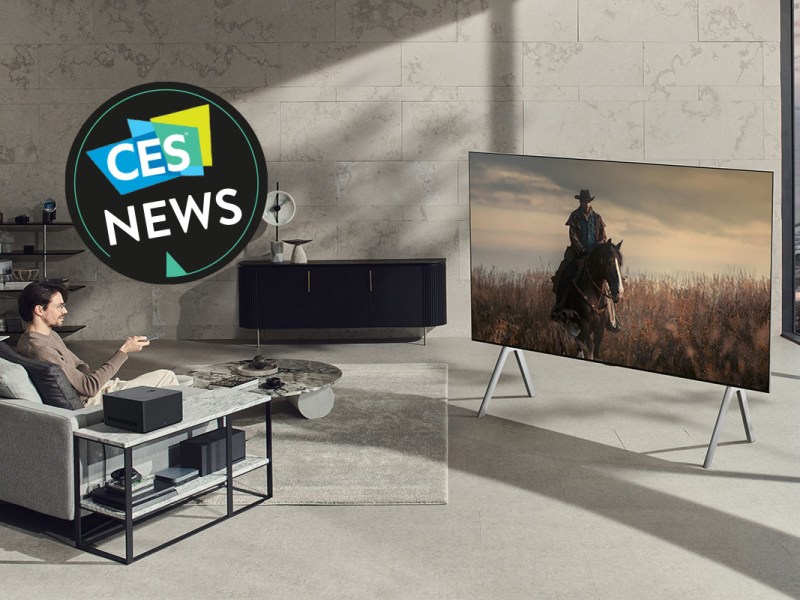 Mann sitz im Wohnzimmer vor einem XXL-OLED-TV, der komplett kabellos angesteuert werden kann.