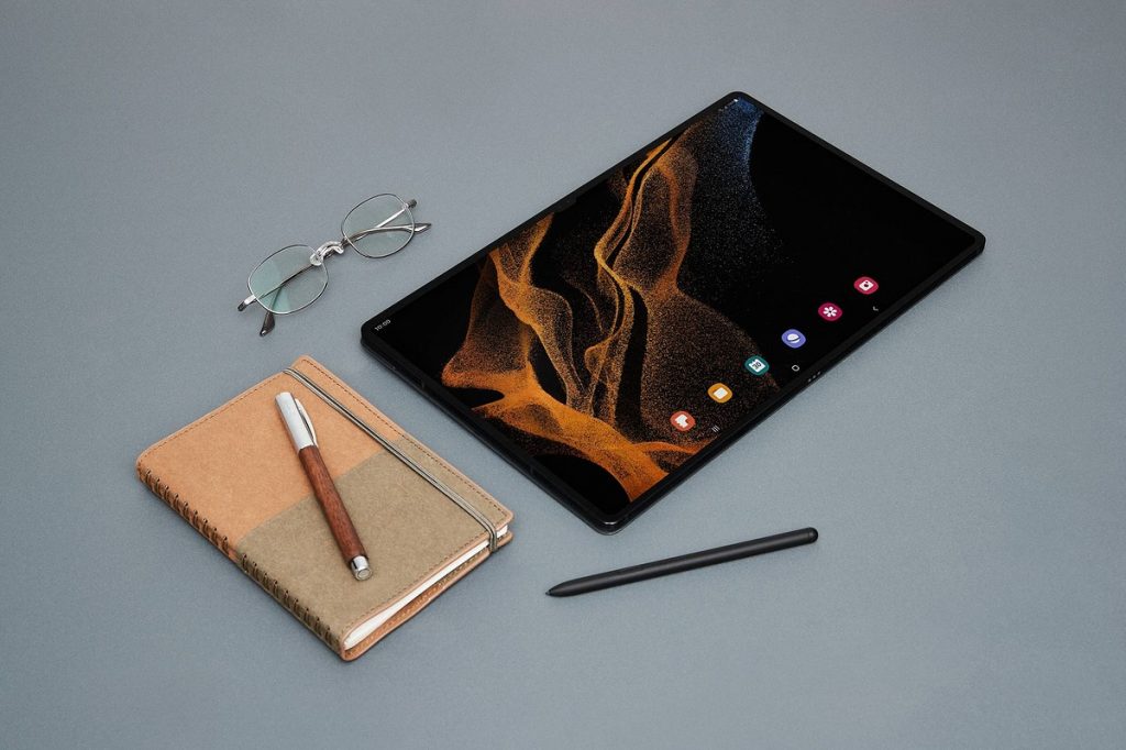 Dunkles Samsung Tablet von oben auf grauem Tisch mit zwei Stiften und hellem Notizbuch