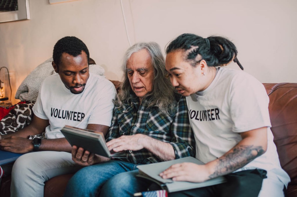 Volunteers schauen mit einem alten Mann ein Buch an.