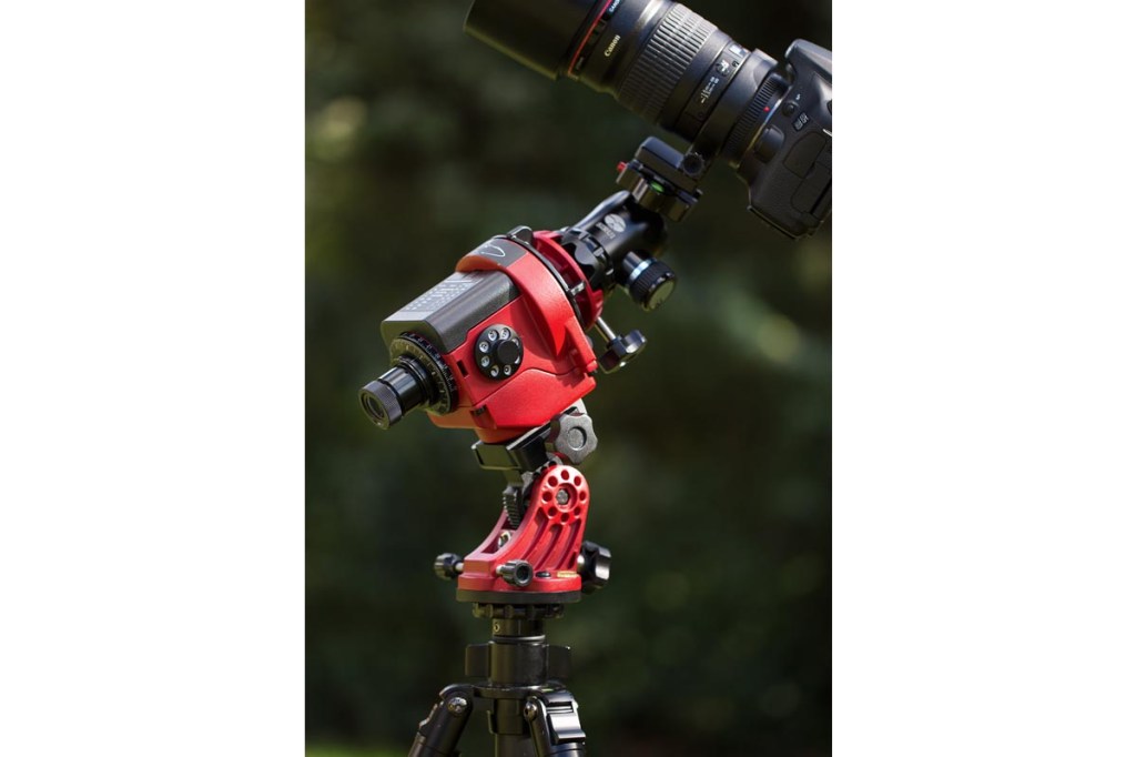 Eine rote-schwarze parallaktische Montierung, die eine Kamera hält. Im Hintergrund verschwimmen Blätter eines Baumes.