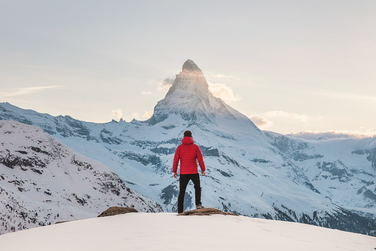 Mann in roter Winterjacke vor verschneitem Berg