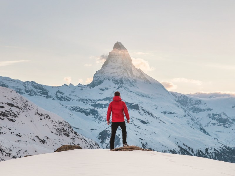 Mann in roter Winterjacke vor verschneitem Berg