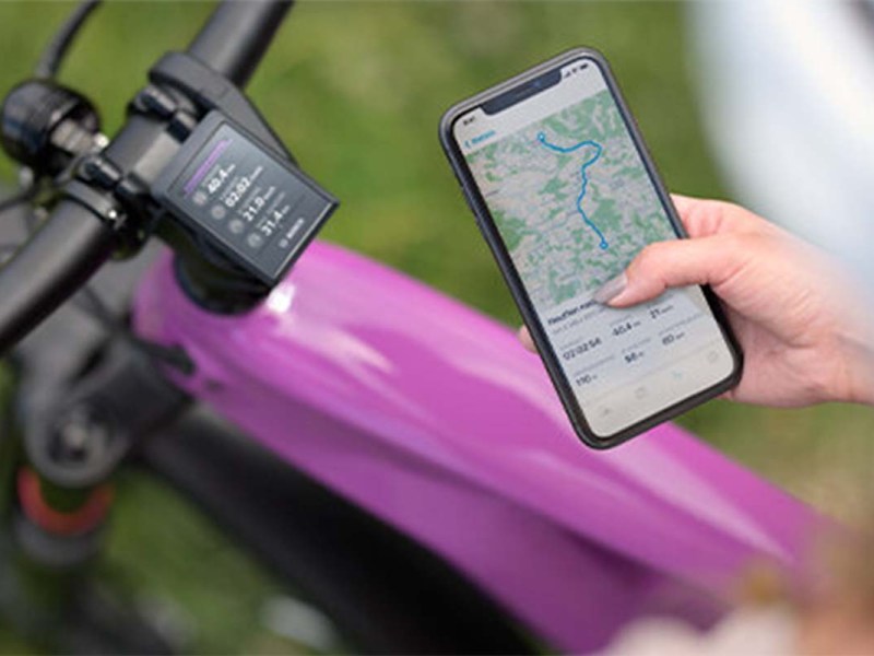 Closeaufnahme: Person hält Smartphone neben das Fahrrad-Display mit Routennavigation