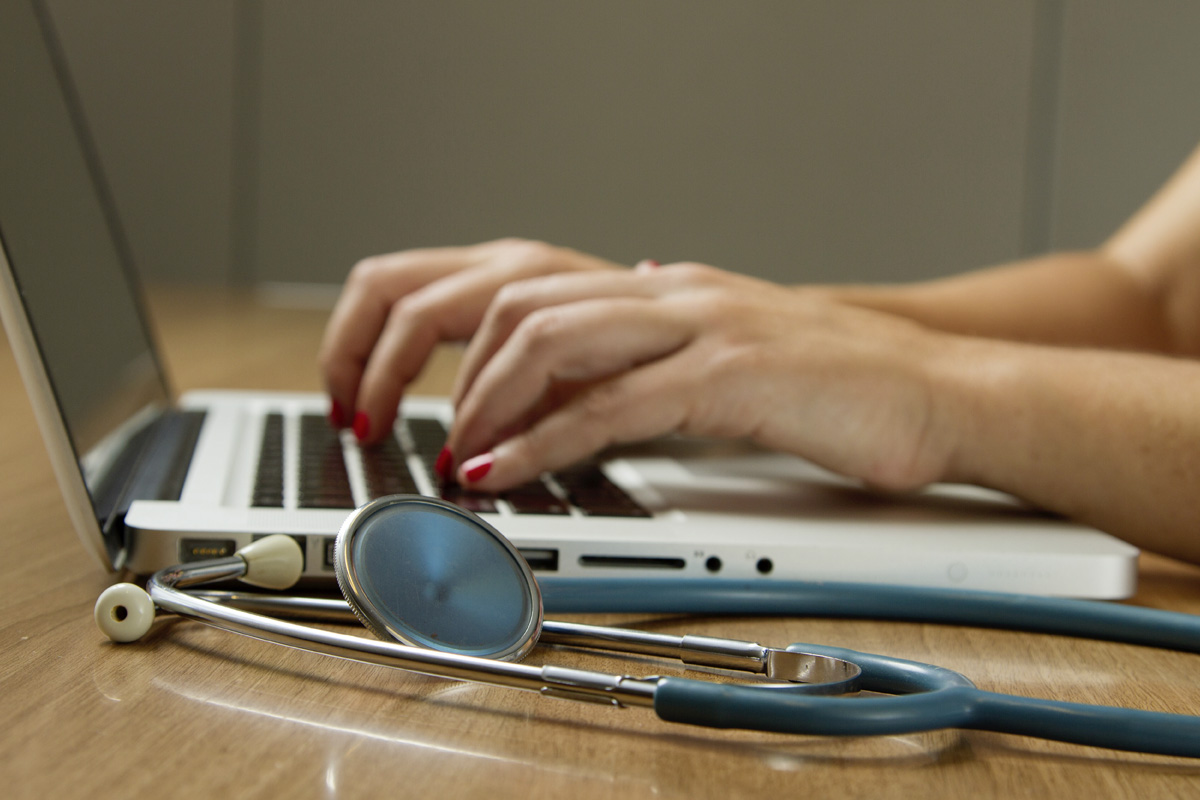 Eine Frau tippt auf einem Laptop, neben ihr liegt ein Stetoskop.