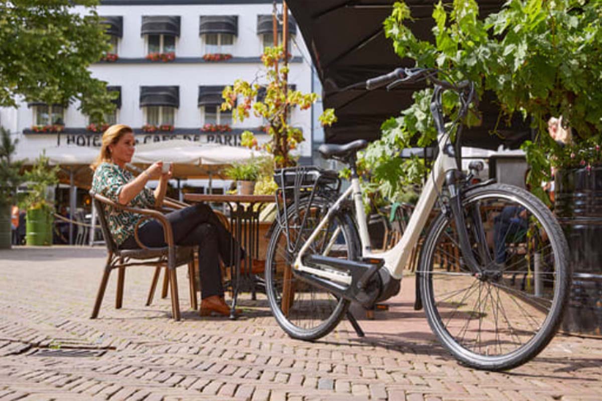 E-Bike von Gazelle im Vordergrund, im HIintergrund sitzt eine Frau im Café
