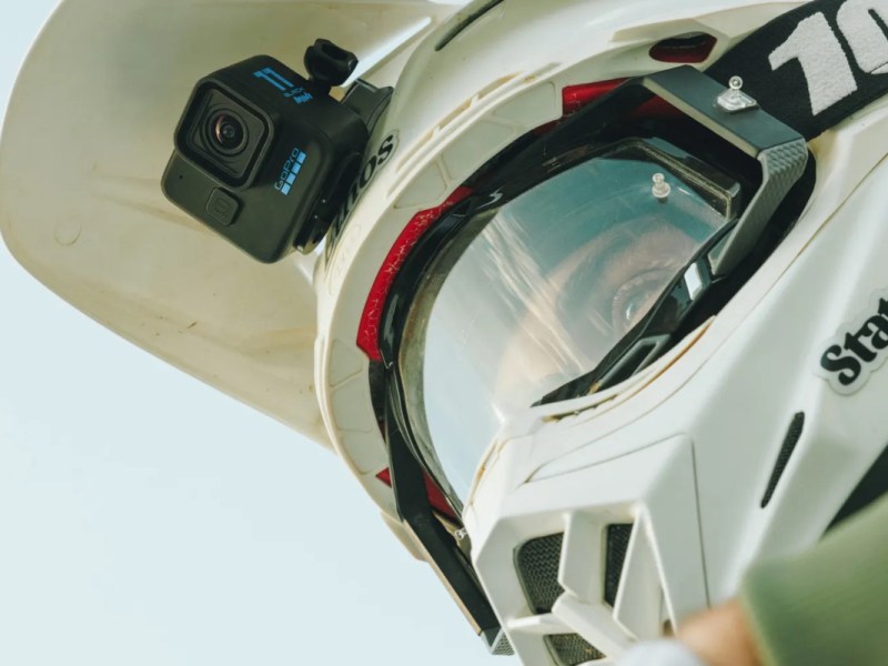 Mann mit weißem Motorradhelm von schräg unten mit schwarzer GoPro-Mini Kamera vorne dran
