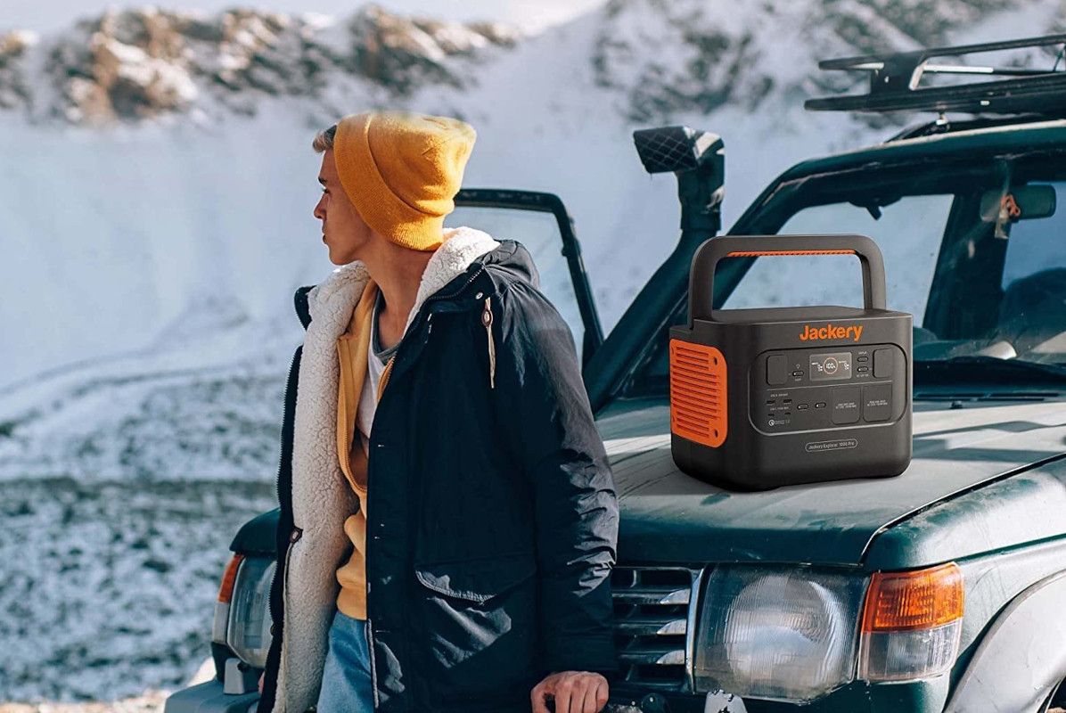 Junger Mann in Winterkleidung lehnt an Offroad-Auto auf dessen Motorhaube eine Jackery Power Station steht in Schneelandschaft