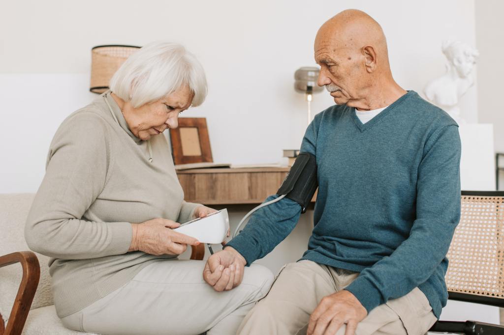 Eine alte Frau misst einem Mann im selbe Alter Blutdruck.