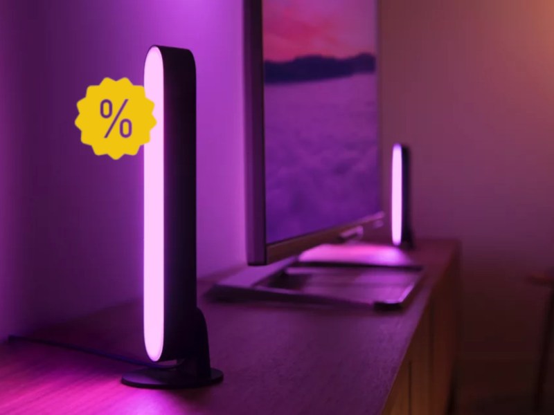 Philips Hue Lightbar pink leuchtend auf Sideboard im Hintergrund Fernseher und weitere Lightbar mit gelben Prozentzeichen links oben