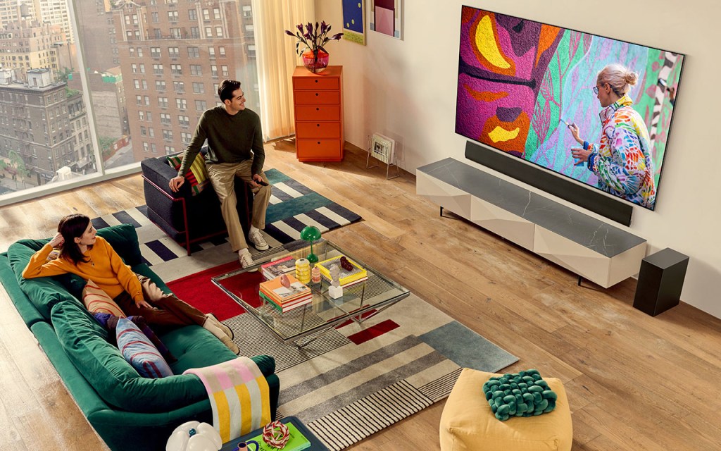 LG OLED evo-TVs: Eine Frau und ein Mann sitzen im Wohnbereich vor einem Flachbild-TV, der an eine Wand montiert wurde.
