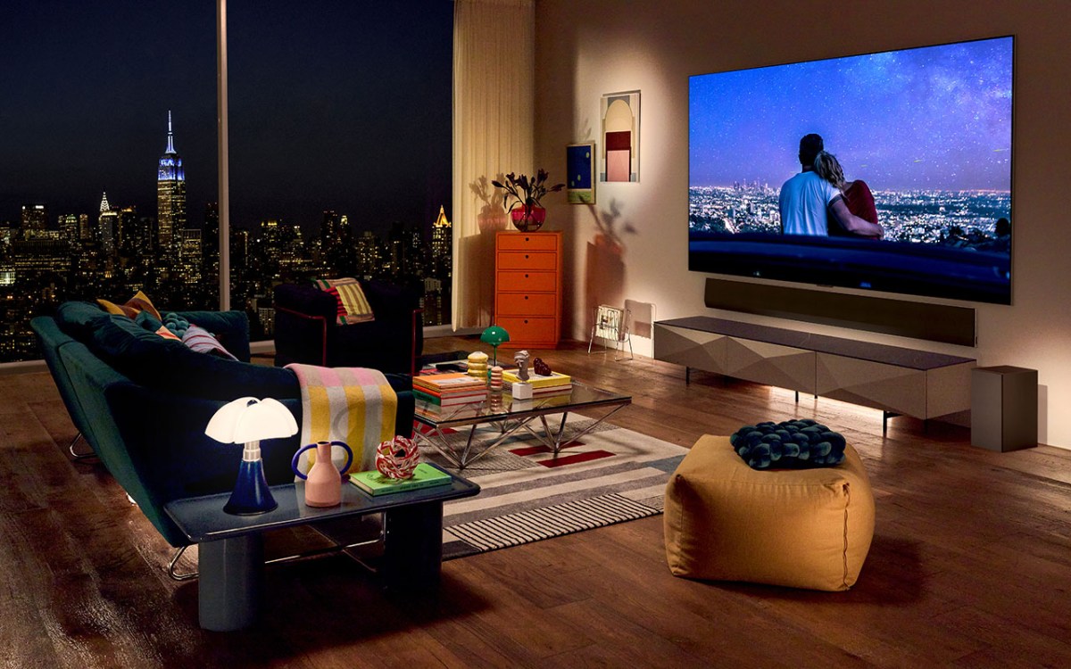 Neue OLED evo-TVs von LG: Flachbild-TV an einer Wand in einer Wohnung.- Davor Sofalandschaft. Im Hintergrund (Fensterblick) ist eine nächtliche Stadtszenerie zu erkennen.
