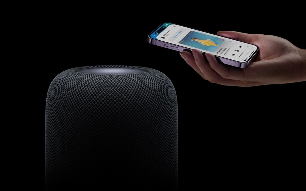 Apple HomePod (2. Generation) wird per Smartphone, das sich in einer Frauenhand befindet, gesteuert.