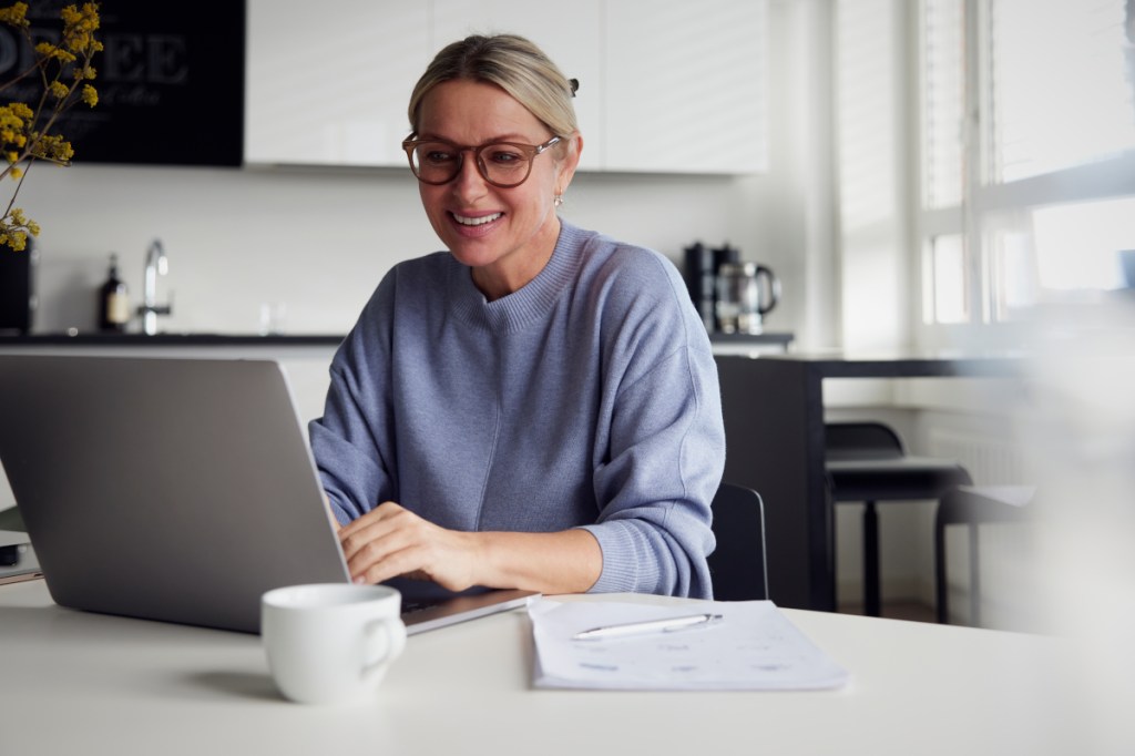 Frau in blauem Sweater sitzt an grauem Notebook an Tisch