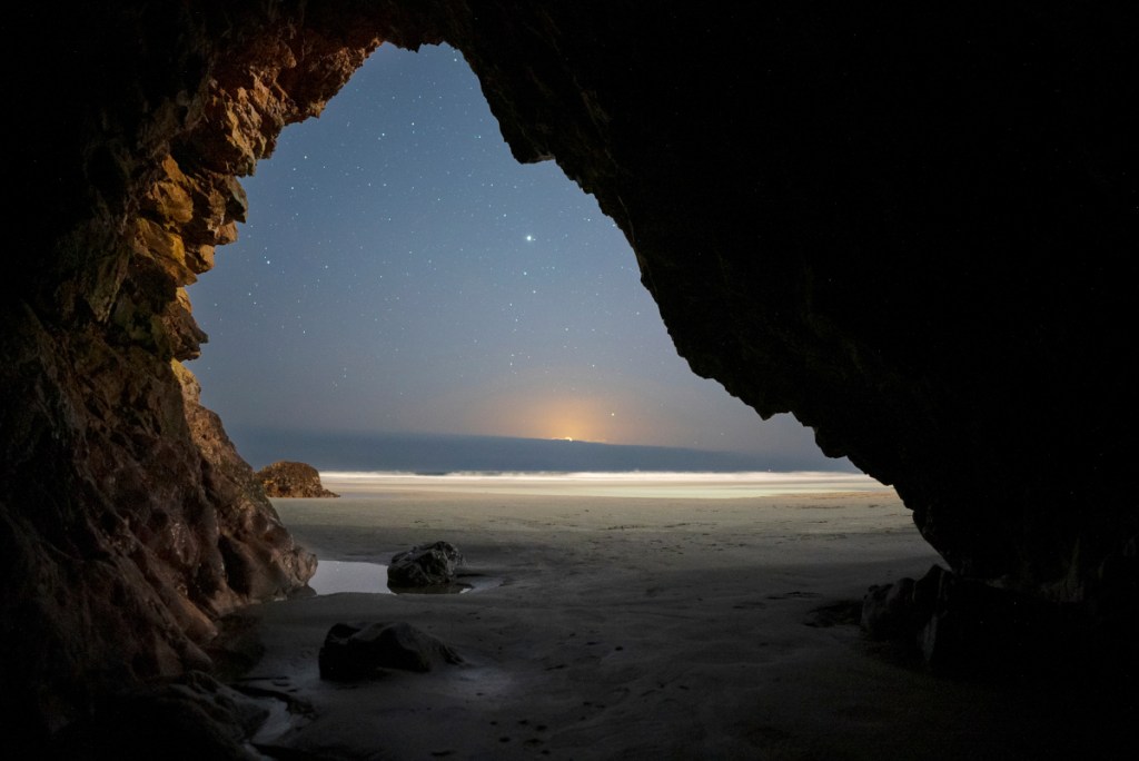 Aus einer Steinhöhle am Strand fotografierter nächtlicher Sternenhimmel.