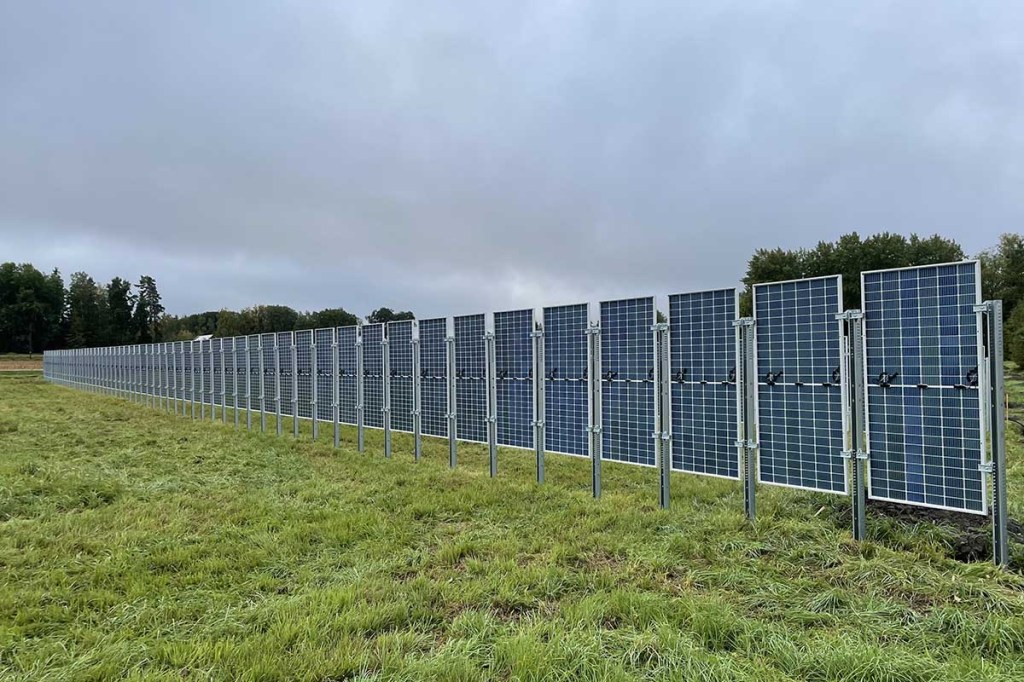 Ein Zaun aus Solarpanels auf einer grünen Wiese.