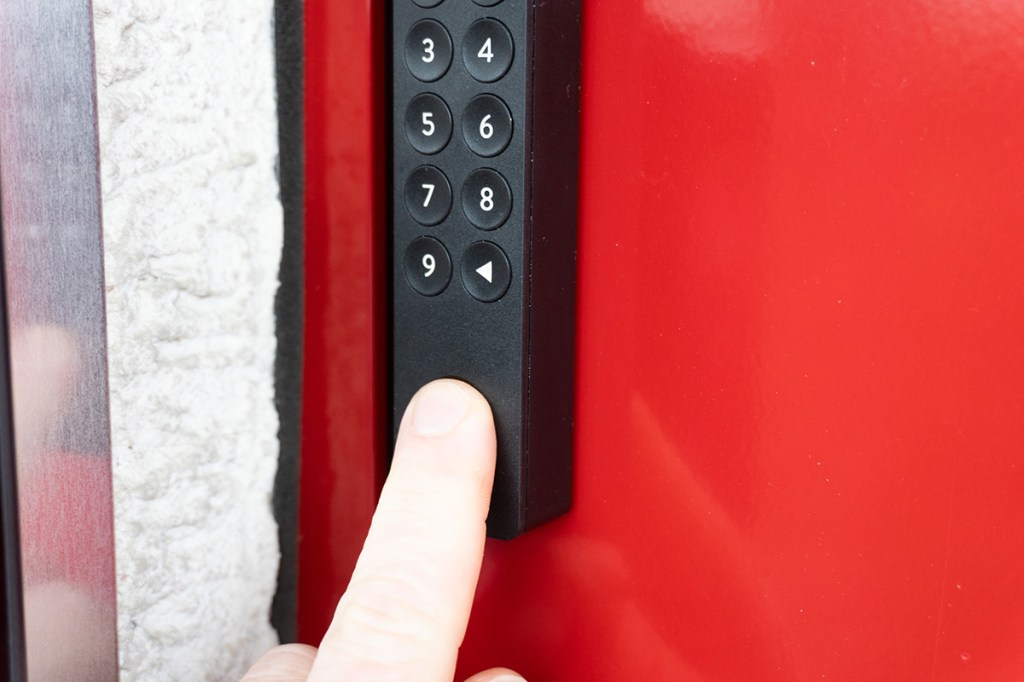 Ein Finger auf dem Fingerprintsensor des Nuki Keypad 2.0, das an einer roten Tür klebt