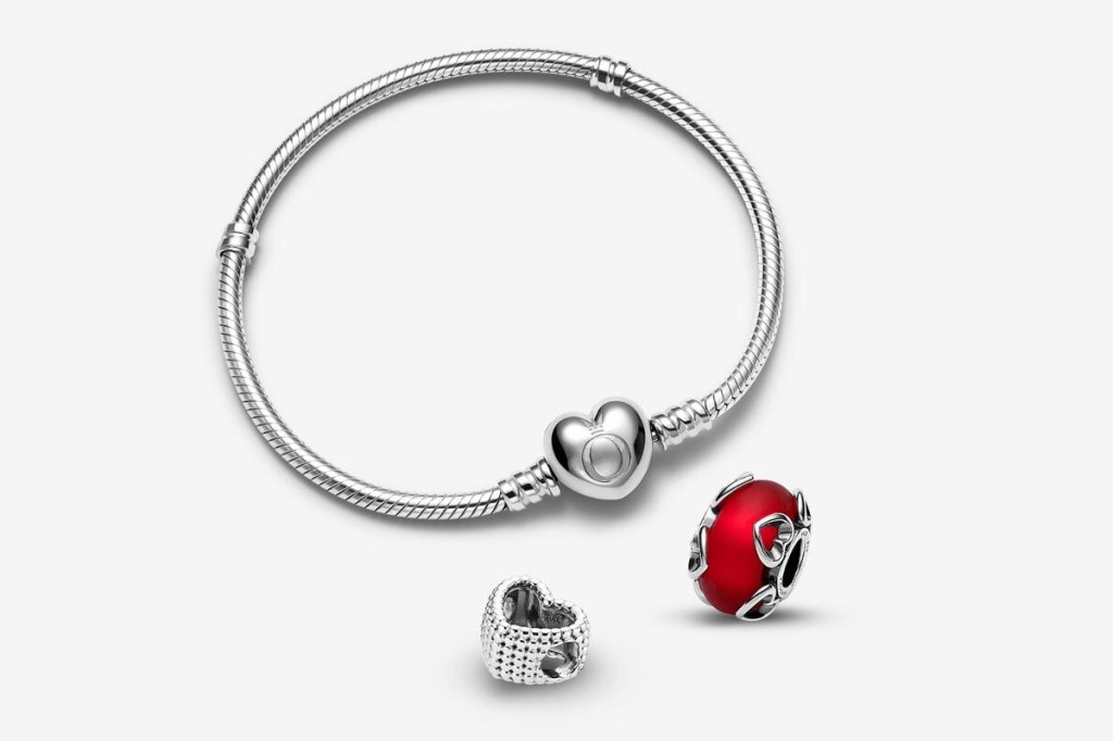 Silbernes Armband mit Herzverschluss, dadrunter roter runder Anhänger und lila Herz auf weißem Hintergrund