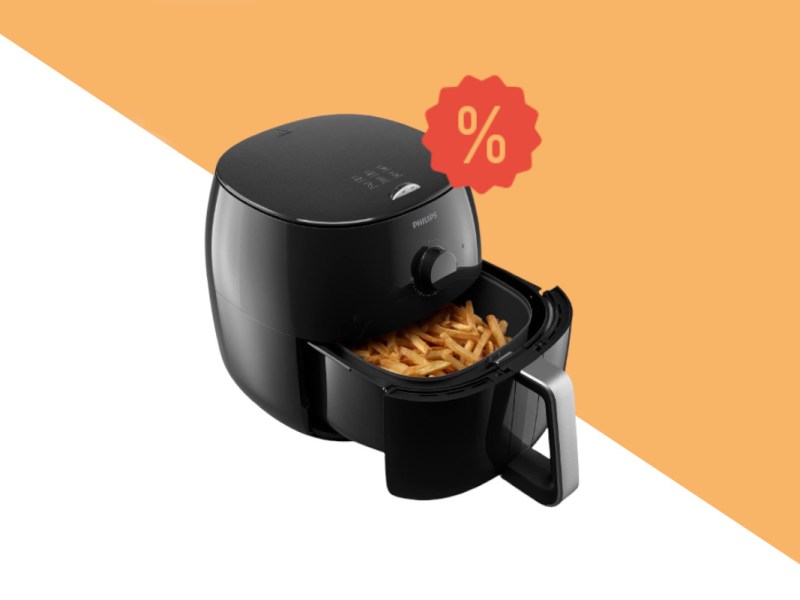 Schwarze Heißluftfritteuse philips Airfryer XXL schräg von vorne mit geöffnetem Korb in dem frittierte Pommes sind auf weiß orangem Hintergrund mit rotem Prozentzeichen rechts oben