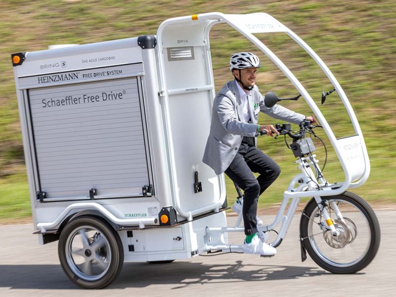 E-Cargo-Bike mit großer Ladebox im Heck und Regenschutz für den Fahrer, Mann fährt auf diesem Bike