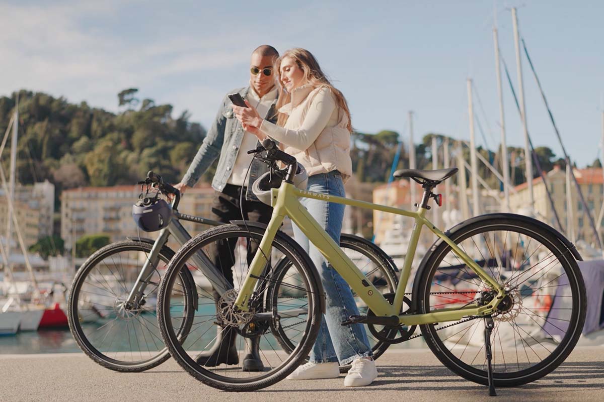 zwei Menschen stehen neben ihren E-Bikes CGOP600 Pro von Tenways und gucken zusammen auf ein Handy, ein Hafen im HIntergrund