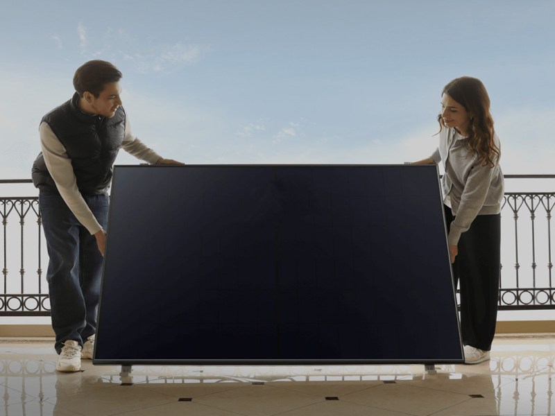 Zwei Personen stehen mit einem Solarpanel auf einem Balkon.